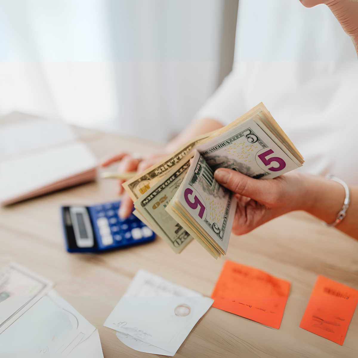 woman holding cash using a calculator at a desk