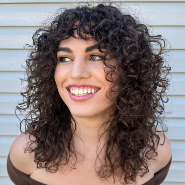 Smiling woman with dark, curly hair featuring layered styling and face-framing fringe, showcasing a low-maintenance haircut for natural curls.