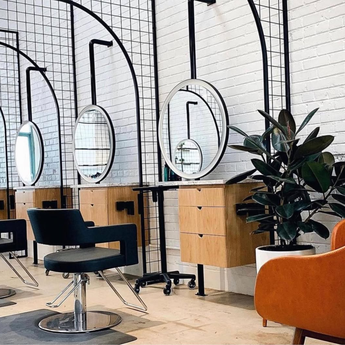 Modern salon interior with black styling chairs, lighted mirrors, and sleek white countertops under decorative pendant lighting.