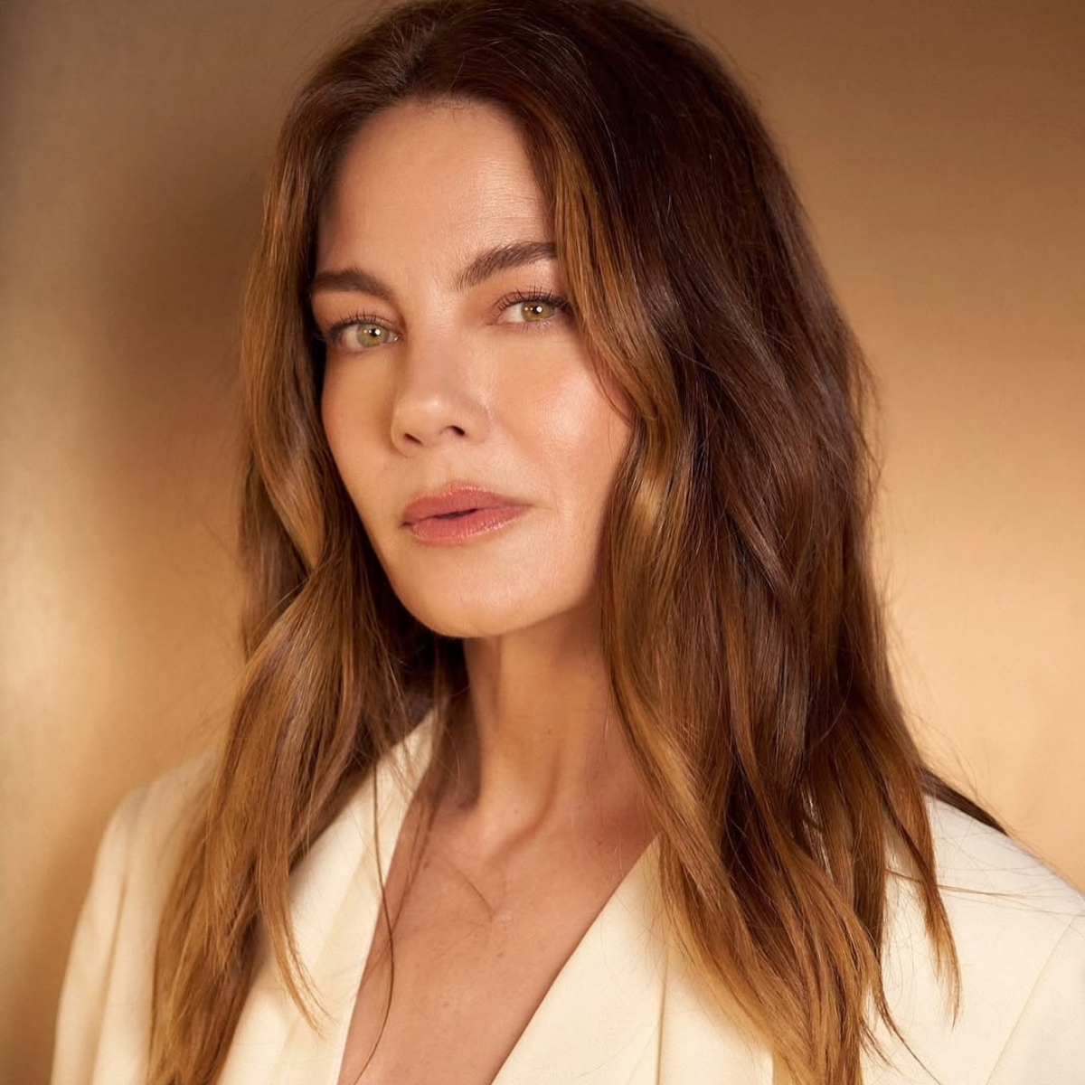 Michelle Monaghan wearing a cream blazer with a rich brunette color and soft golden tones